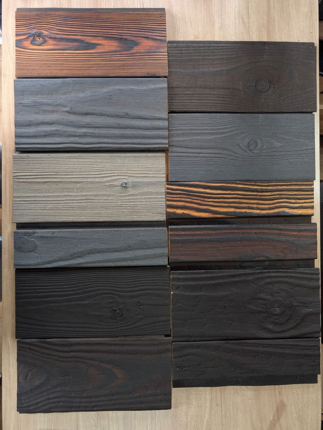 Samples of charred wood in different finishes, laid out on a wooden table.