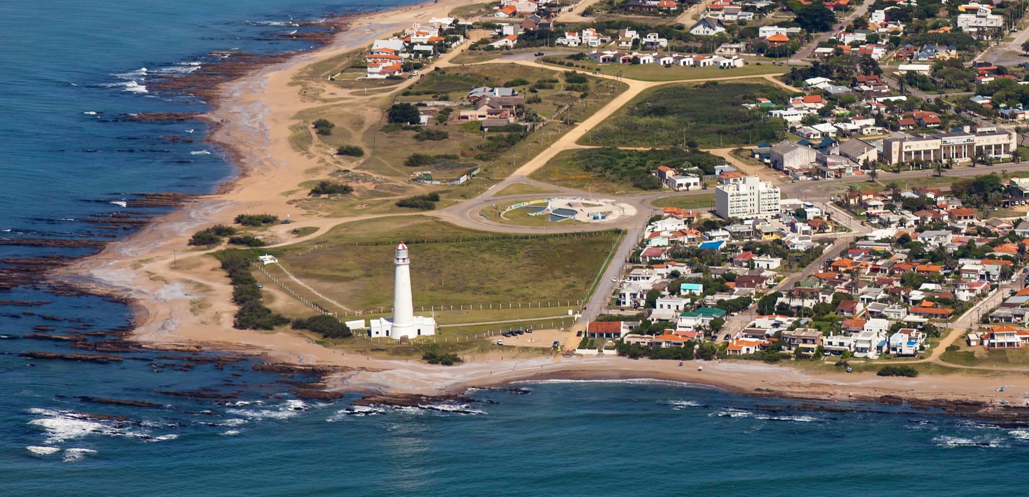 Aerial view of the coast at La Paloma: the white lighthouse by the sea, sandy beaches and houses among greenery.