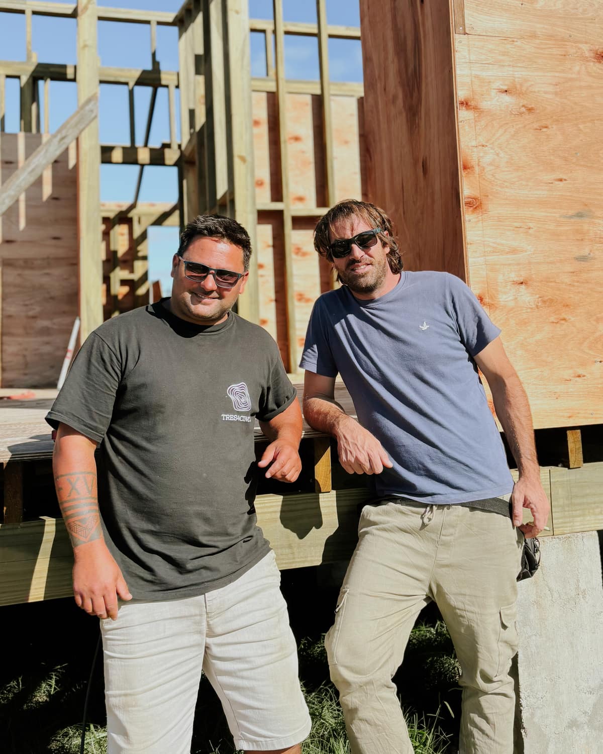 Carlos Olivera and Ramiro García in front of the timber frame of a house under construction