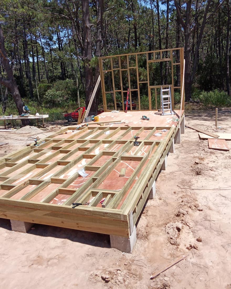 Timber floor frame on the piers, the first wall already standing behind it.