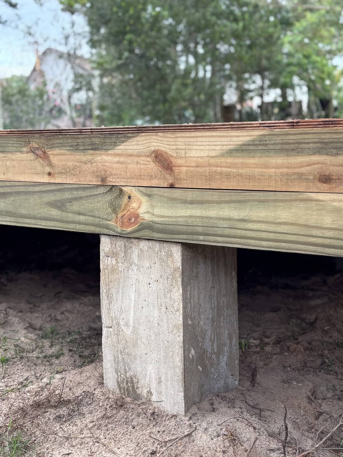 Close-up of the edge of an impregnated pine beam on a concrete pier, with the grain and knots clearly visible.