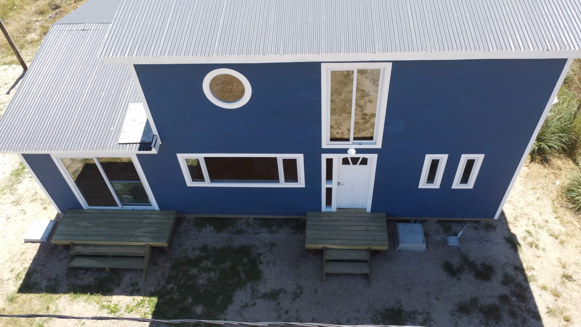 Casa Azul from the air, at an angle: dark gable roof, round porthole window and the front timber terrace with benches.