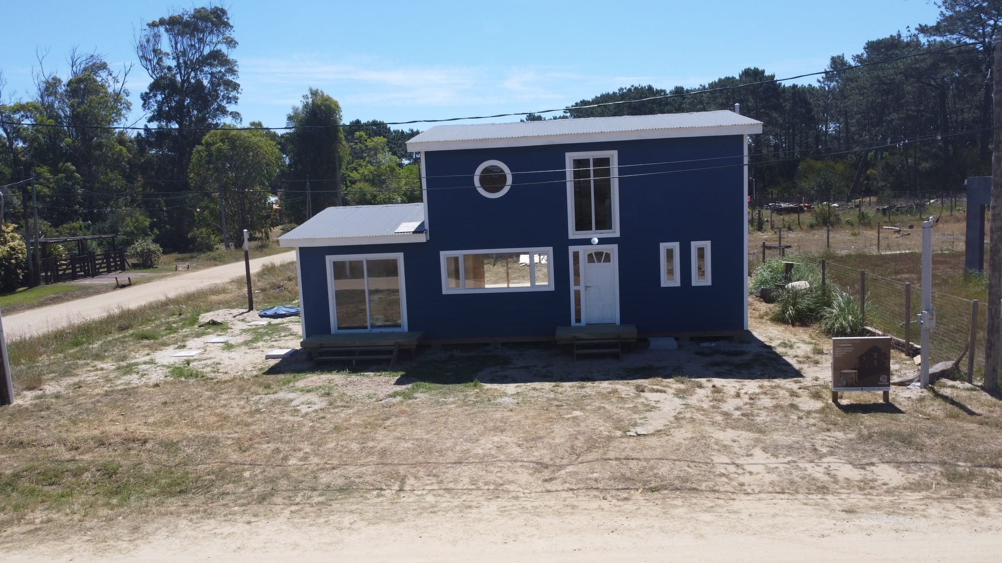 Casa Azul from the front at low height: the plot, the sand road and the pines behind.