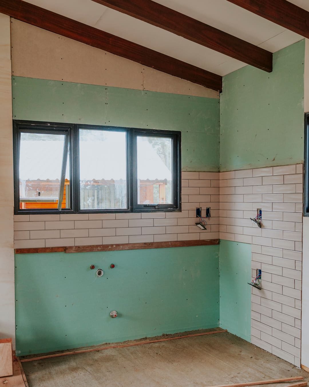 Kitchen corner in progress: green moisture-resistant boards, white wall tiles half set, a window above.