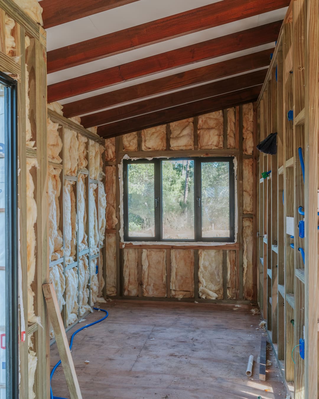 Insulated room with a window and open studs, blue conduits running along the floor.