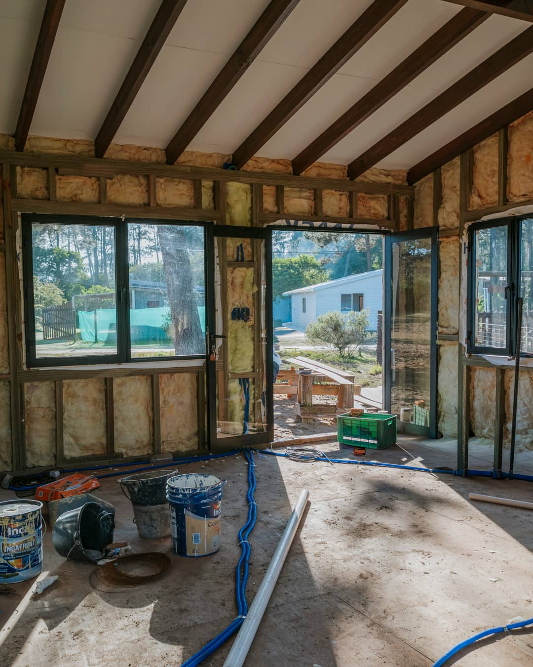Interior at shell stage: insulation between the timber studs, dark roof beams, windows fitted, tools and buckets on the floor.