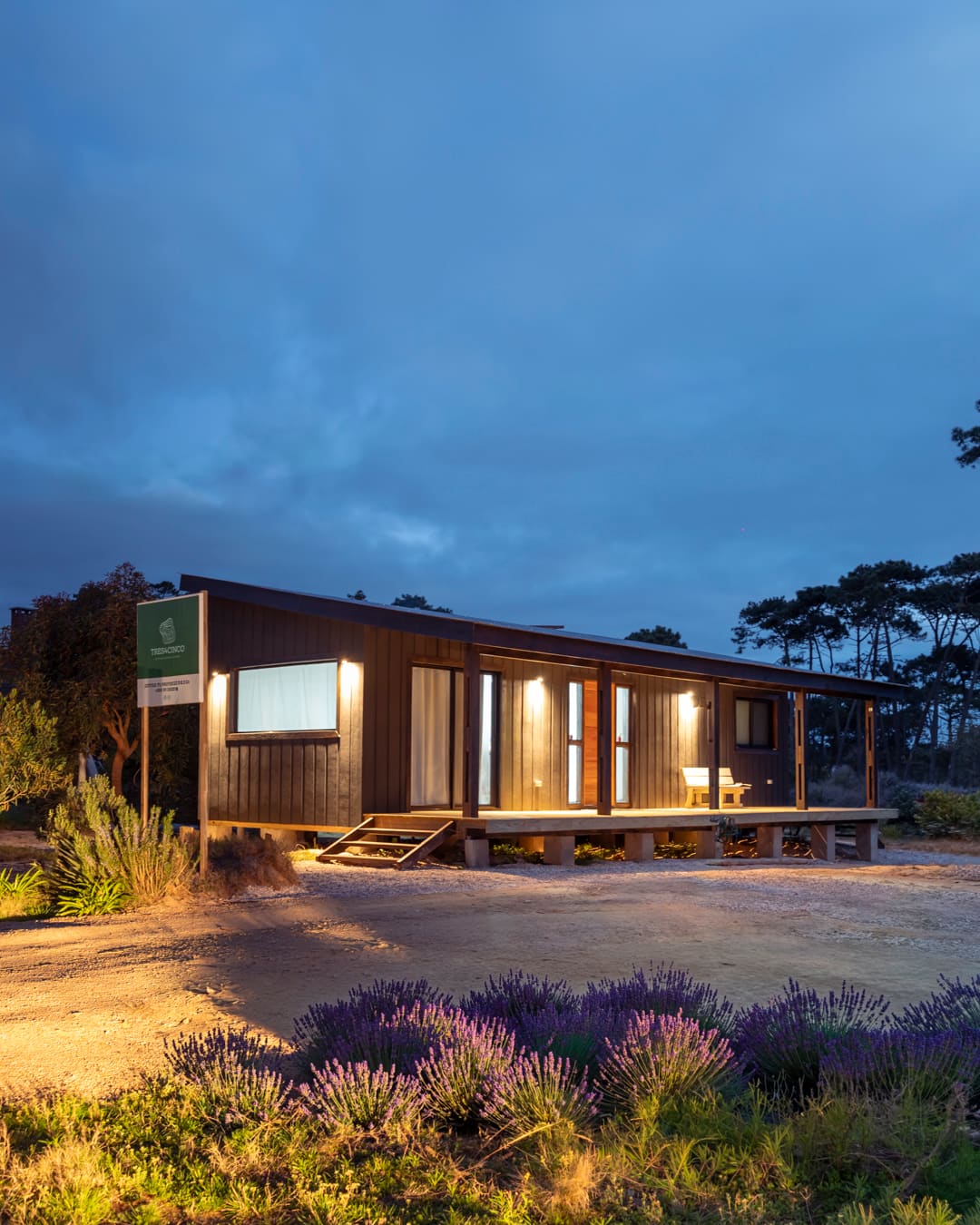 La Peregrina at dusk: black facade, the veranda's outdoor lights on, pines behind.