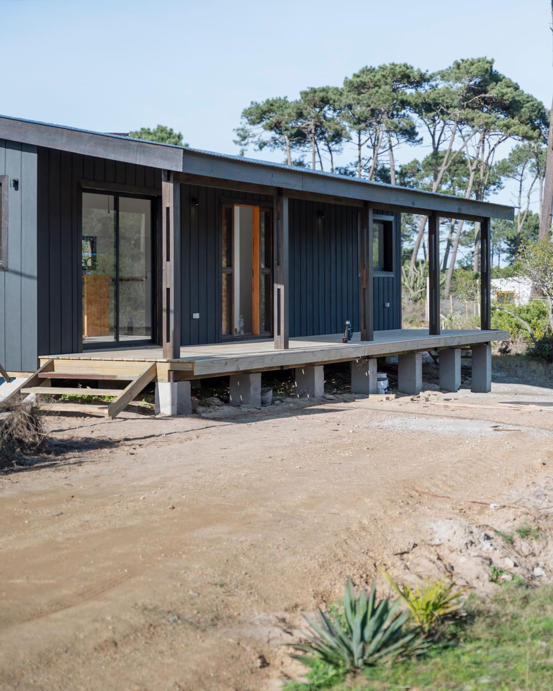 Veranda on concrete piers with timber steps, behind it the sliding door and entrance in the black facade.