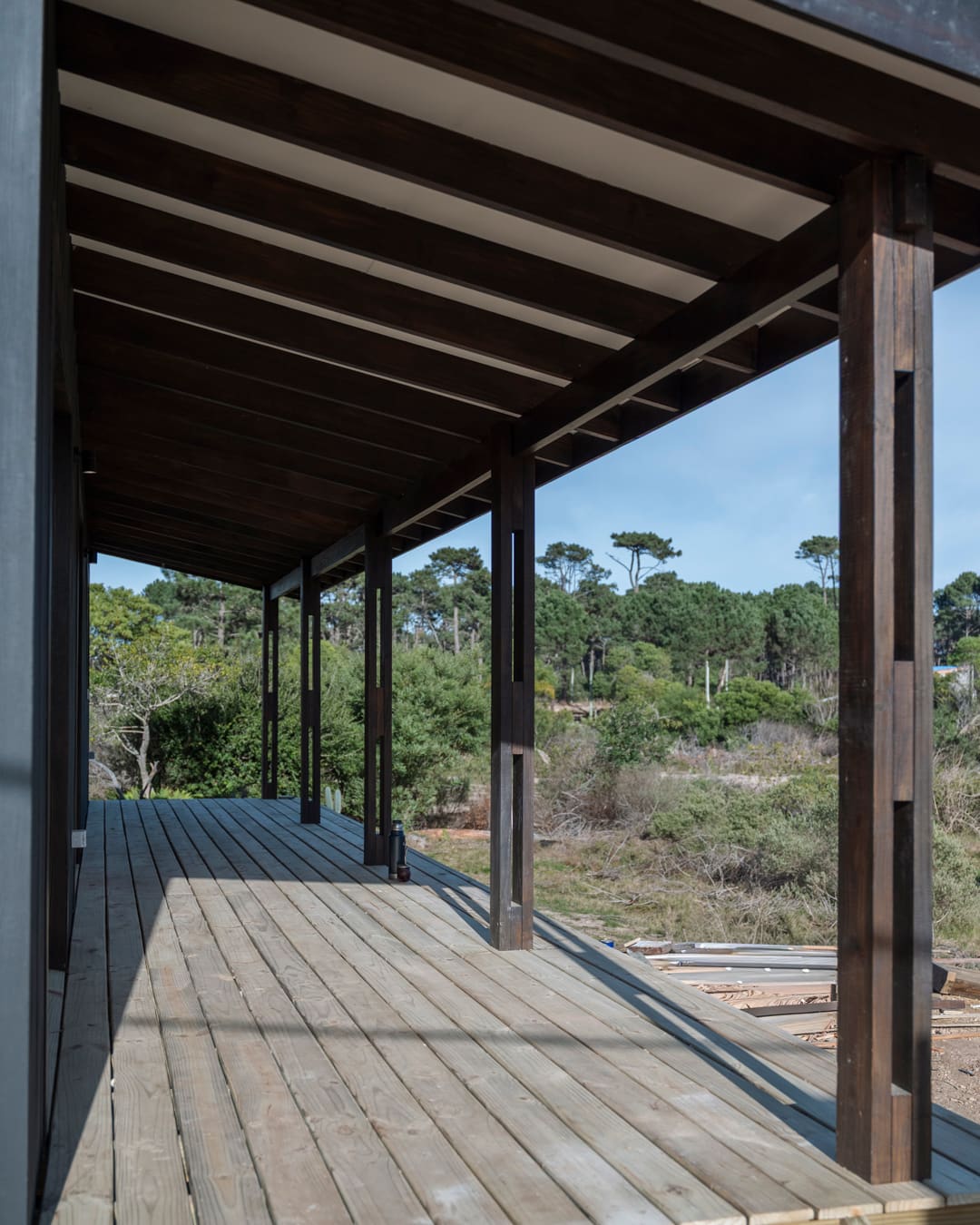 Covered veranda with dark timber posts and roof beams, looking along the deck into the green.