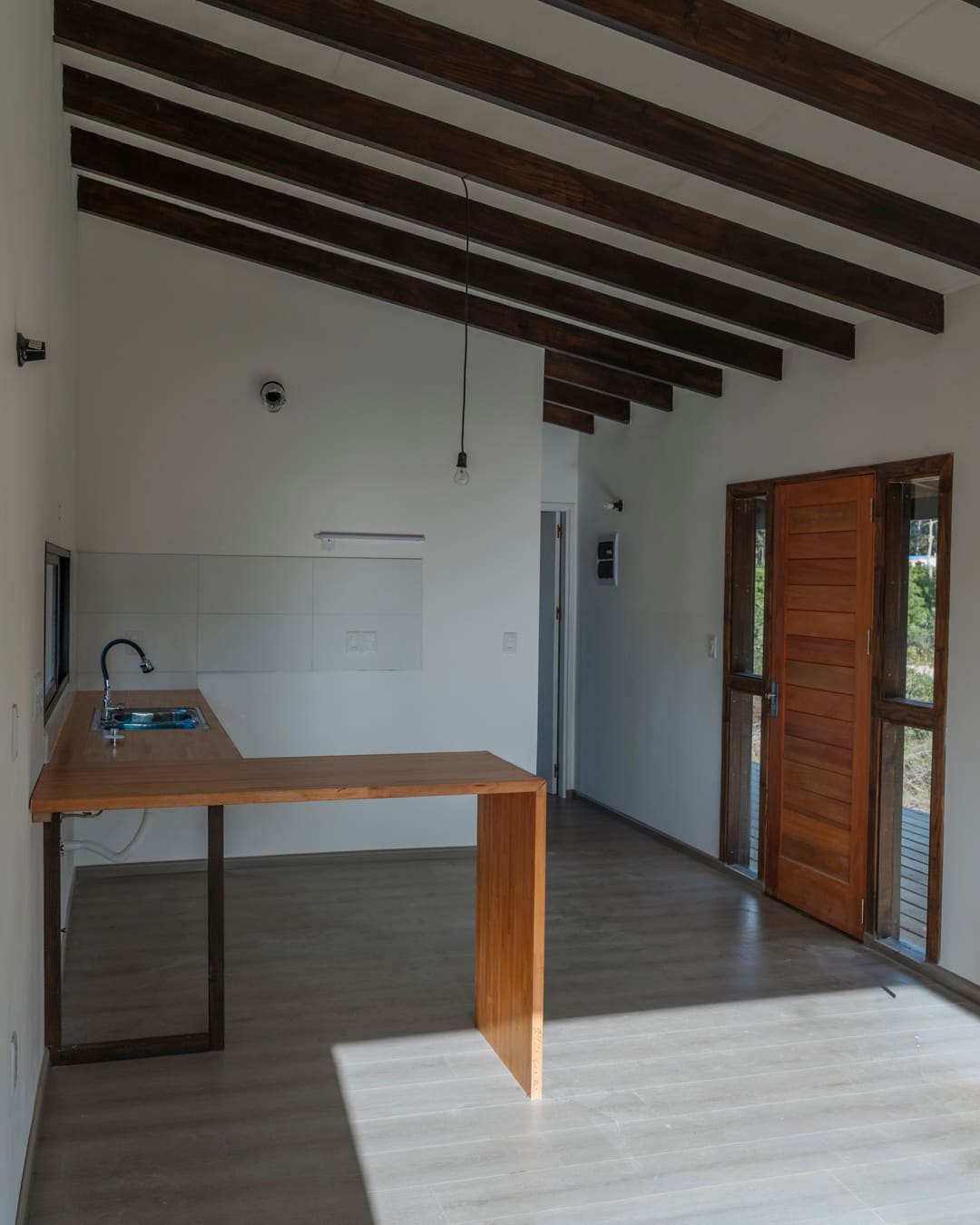 Kitchen with an L-shaped timber counter under dark roof beams, the timber front door on the right.