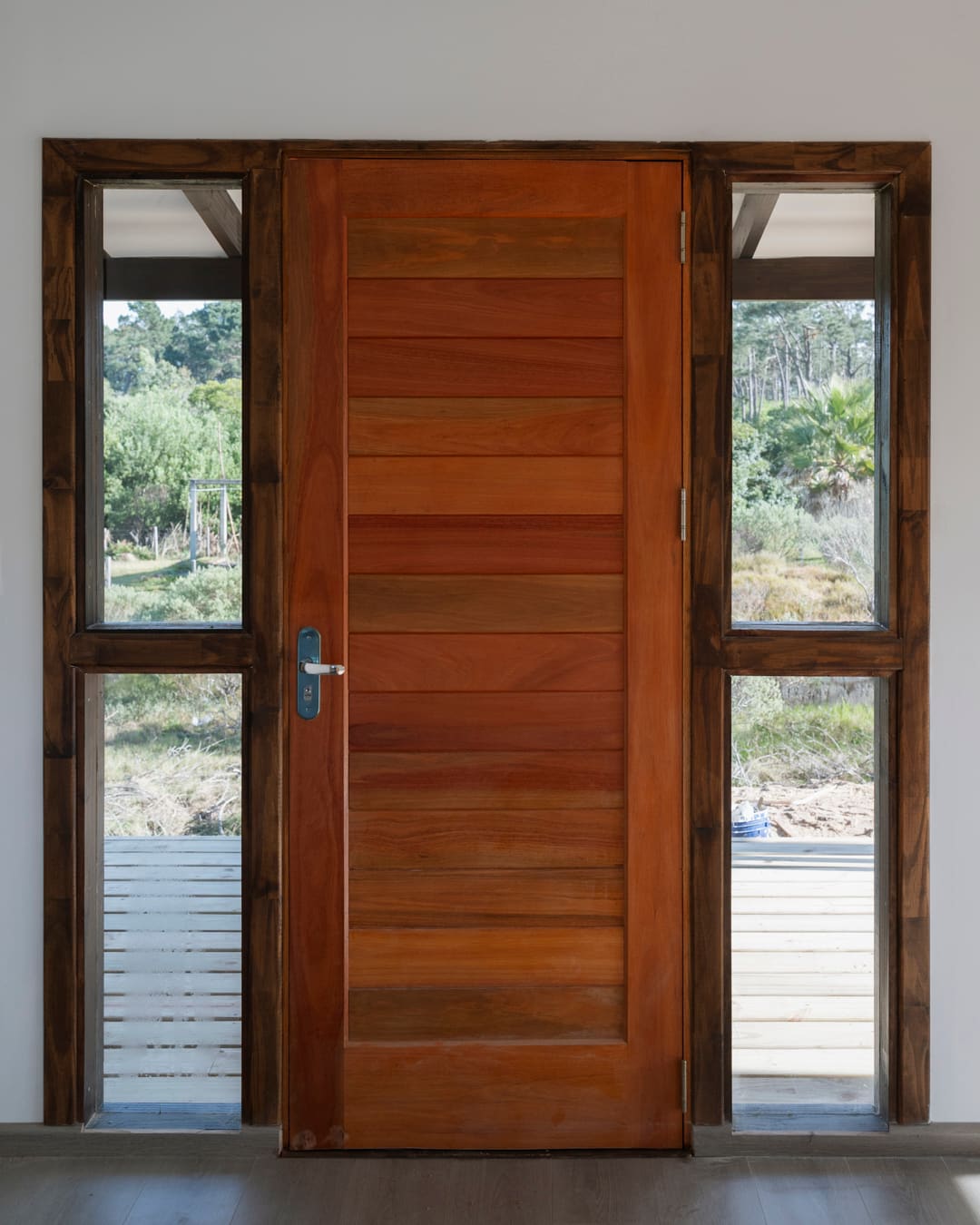 Timber front door from inside, glazed side panels left and right with a view of the veranda.