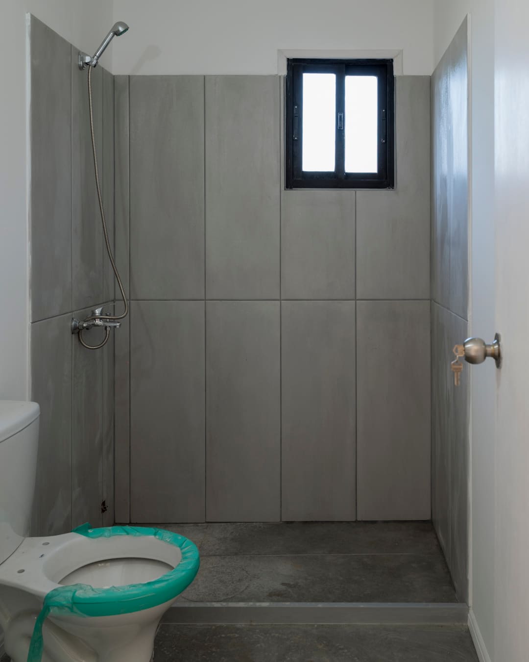 Shower with large grey tiles and a small window.