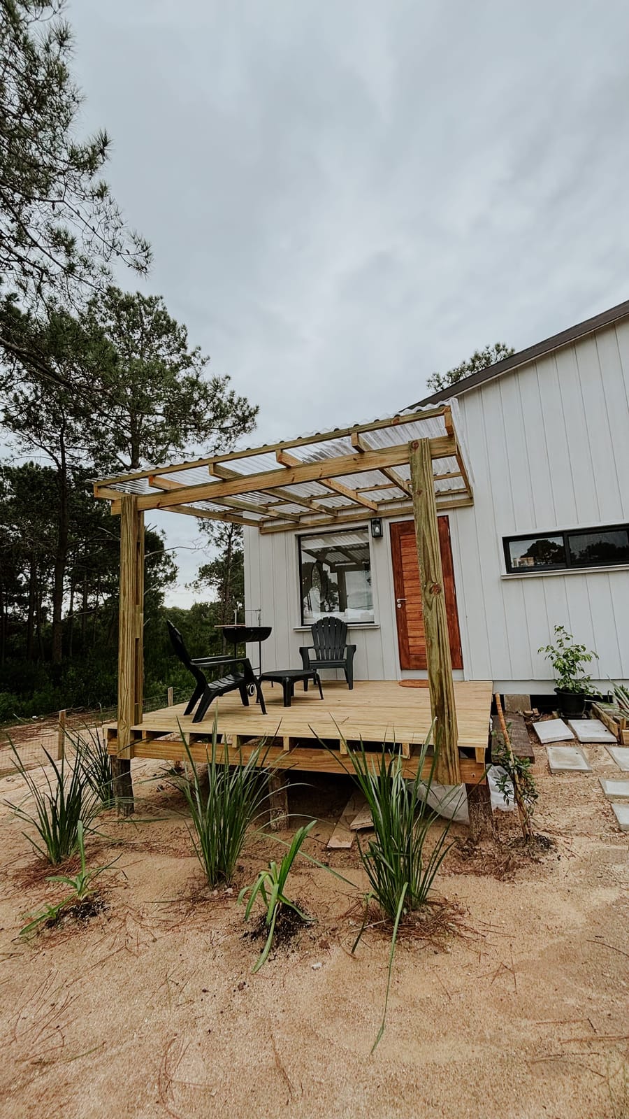 Finished terrace with pergola at Matipipe: white facade, orange front door, garden furniture and pine forest in the background.
