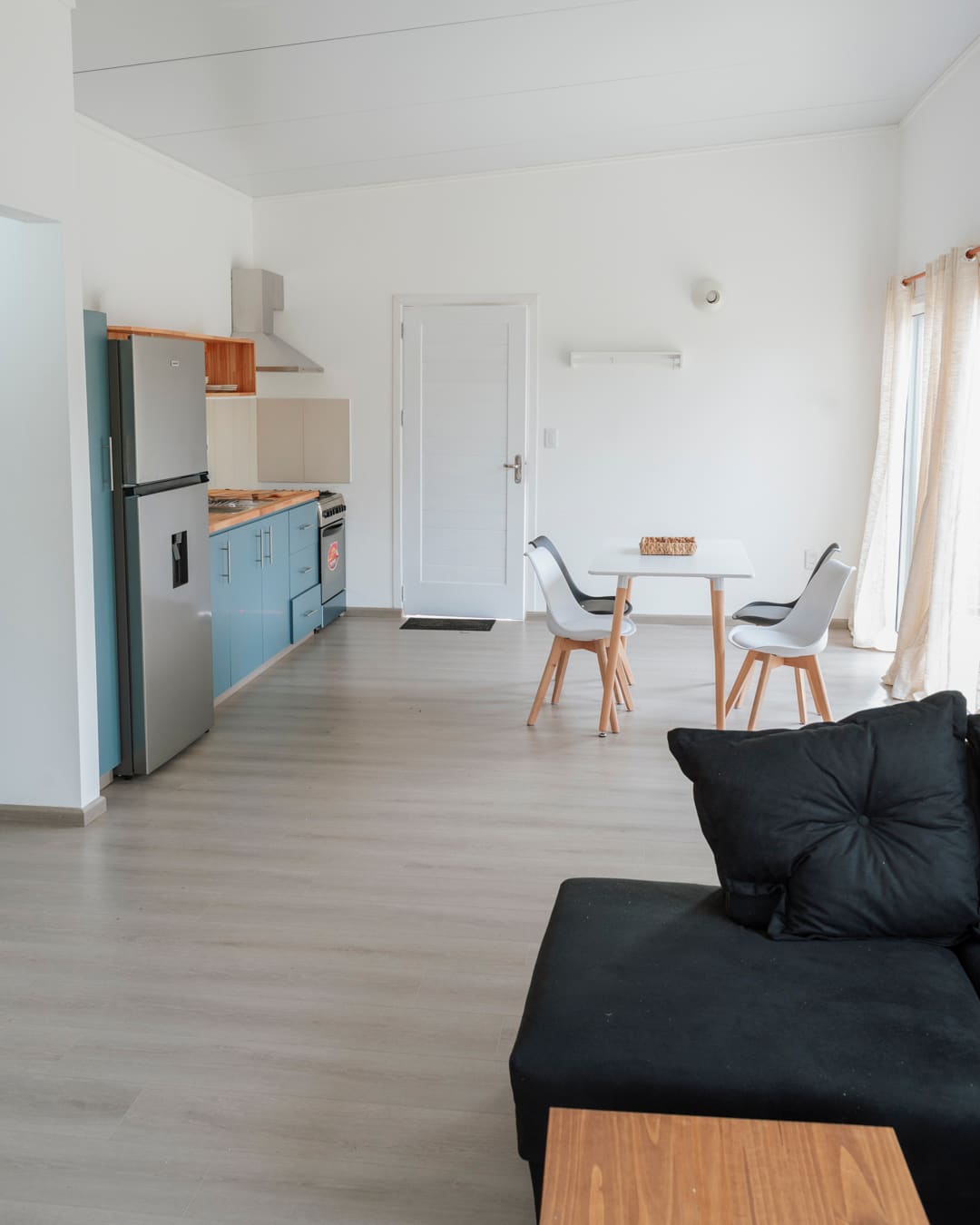 Furnished open living space with a black sofa, a dining table with chairs and the kitchen along the left wall.