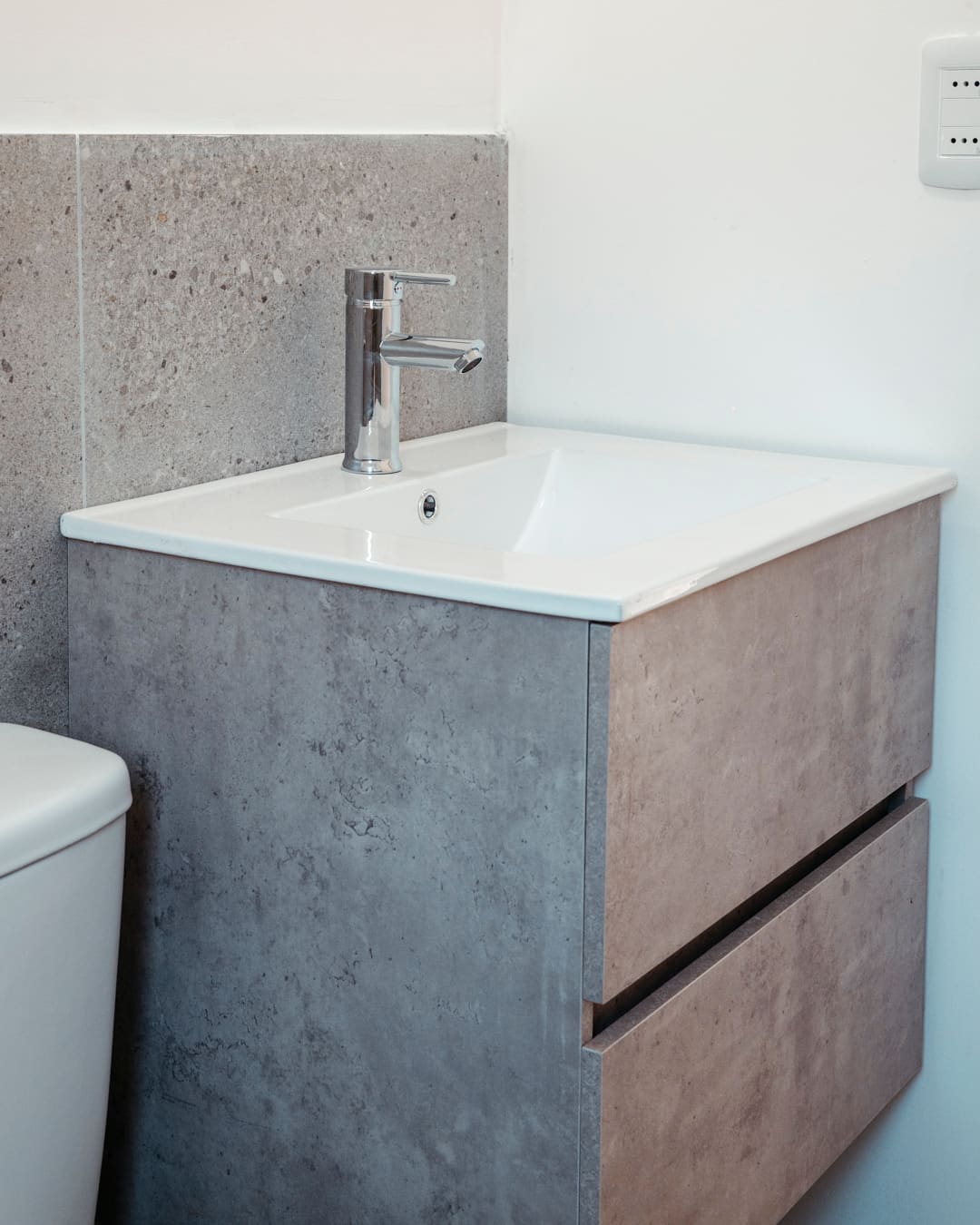 Wall-hung concrete-look vanity with drawers, white basin and tap, a toilet at the left edge.