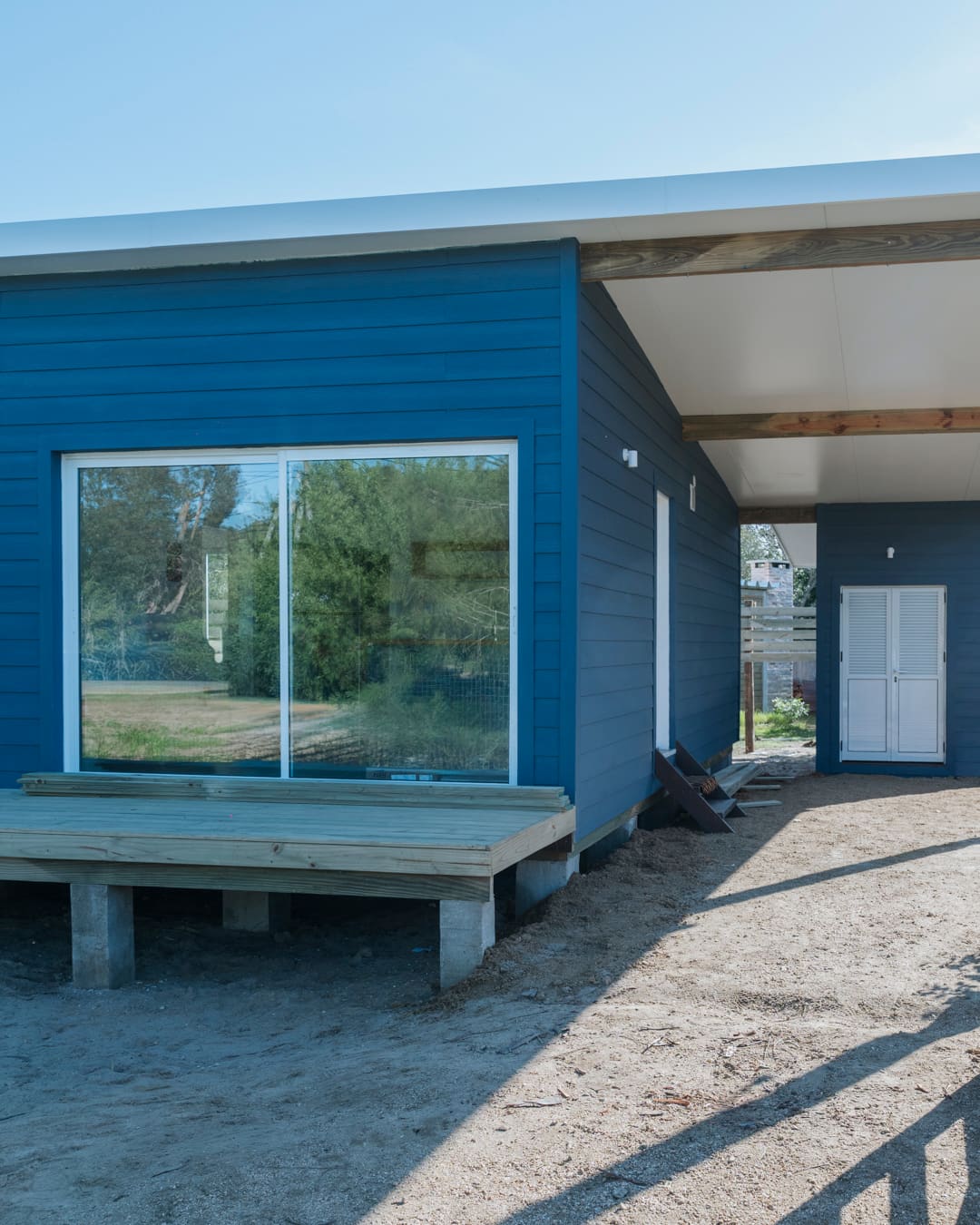 Blue facade with a large sliding glass door and deck, and a covered way leading to a white louvered door.