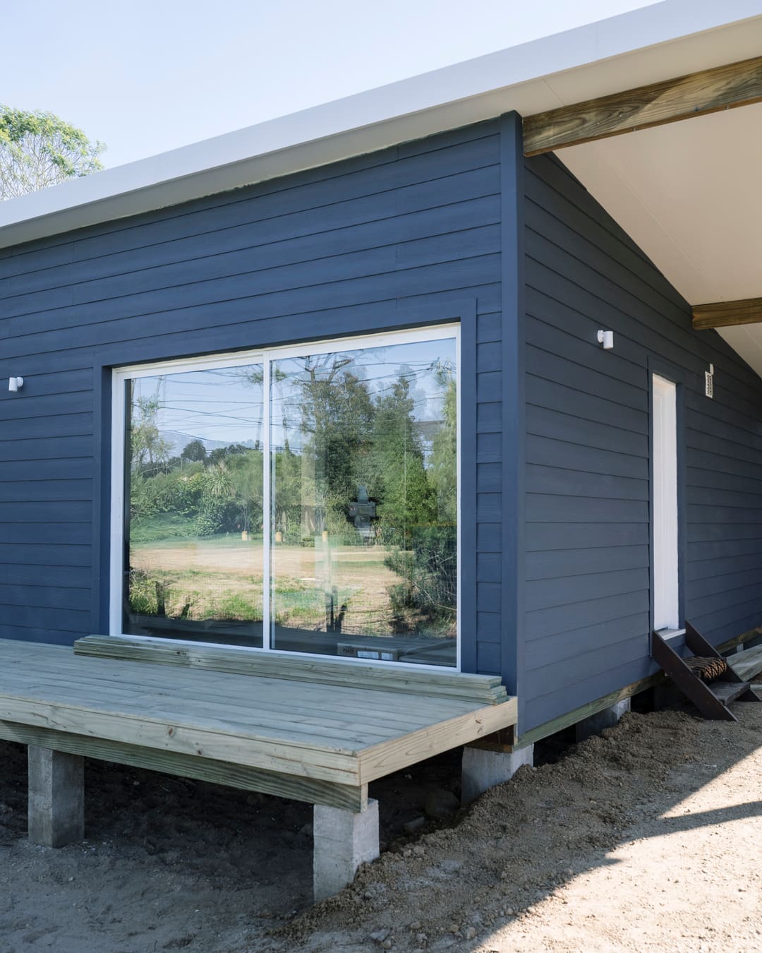 Dark blue facade with a large sliding glass door reflecting trees, and a timber deck in front.