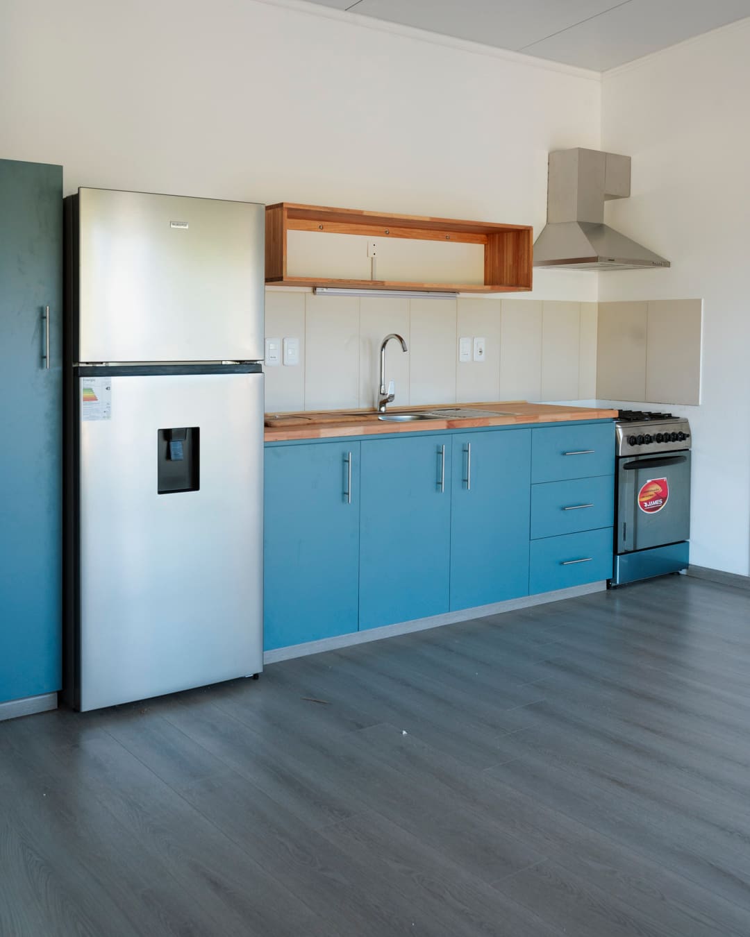 Kitchen with teal cabinets, a wooden worktop, sink, hob, cooker hood and a stainless steel fridge.