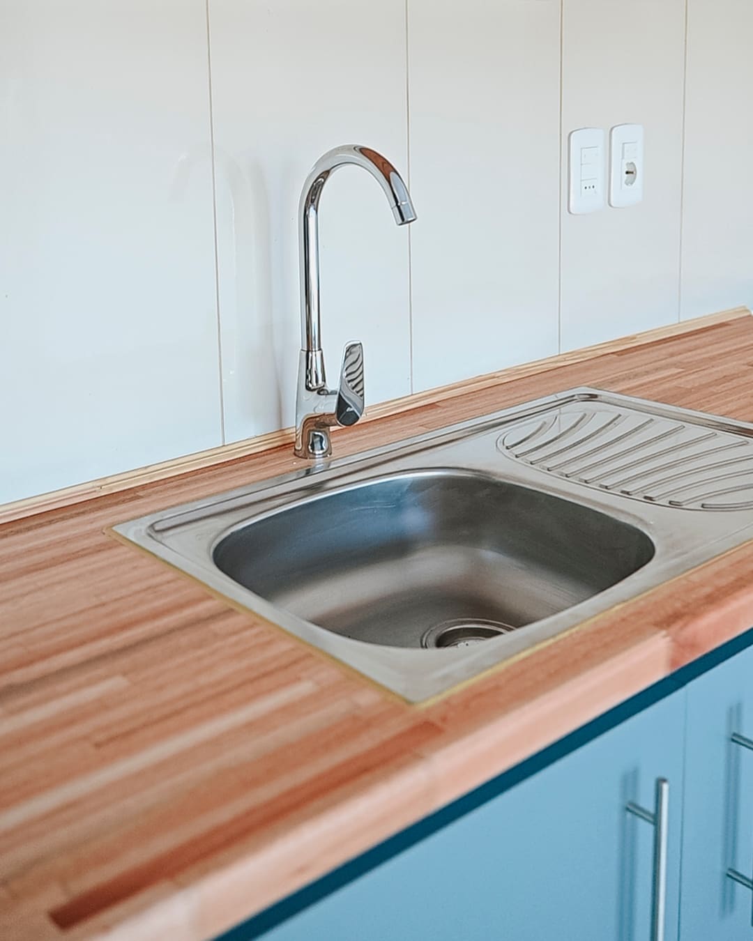 Stainless steel sink with a tall tap set in a wooden worktop, teal cabinet doors below.